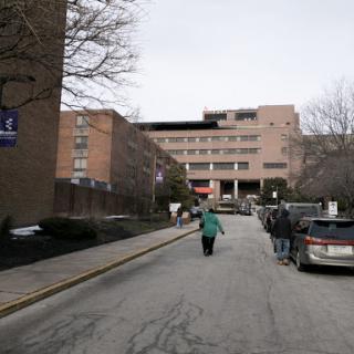A view of a hospital building along a street, with a person walking towards the entrance.