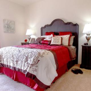 A cozy bedroom with elegant red and white bedding and classic wooden furniture.