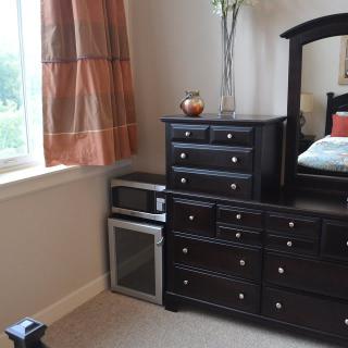 A cozy bedroom corner featuring a dresser with a mirror, adjacent to a window with draped curtains.