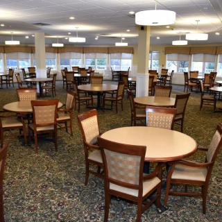 A spacious dining area with multiple round tables and chairs arranged neatly under ceiling lights.