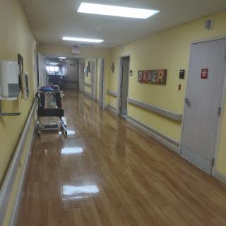 A view of a hospital hallway with yellow walls and polished floors, featuring a patient cart.