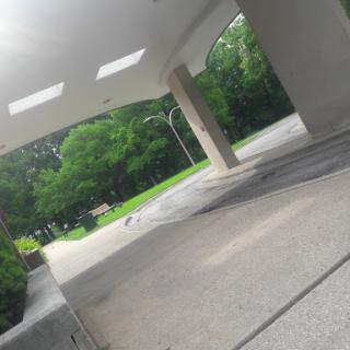 A serene walkway under a modern architectural structure, surrounded by lush greenery.