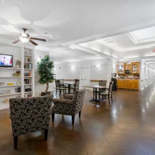 A cozy and well-lit living space featuring comfortable seating, a television, bookshelves, and a kitchenette.