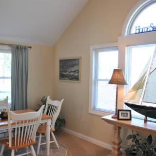 A cozy dining room with a table and chairs, decorated with a lamp and art near large windows.