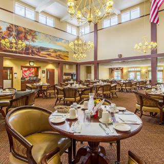 A spacious dining hall with elegantly set tables, ornate chandeliers, and mural decorations on the walls.