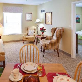 A cozy living room and dining area featuring comfortable chairs, a small dining table with place settings, and warm lighting.