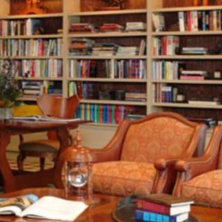 A cozy library with bookshelves, armchairs, and a wooden table, providing a comfortable reading area.