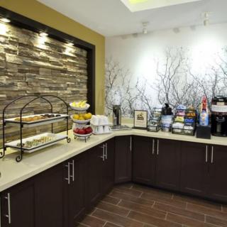 A well-lit breakfast area in a hotel featuring a variety of snacks, coffee machines, and a buffet setup.