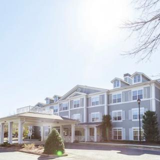 A sunny view of a residential building with a light blue facade and landscaped surroundings.