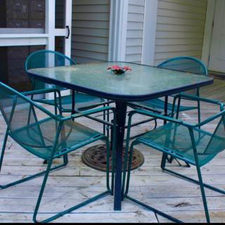 A set of outdoor patio furniture with a glass table and four metal chairs on a wooden deck.