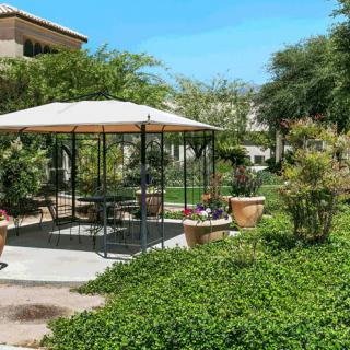 A tranquil garden setting with a gazebo and outdoor furniture, surrounded by lush greenery.