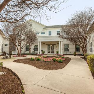 A welcoming entrance to a residential building with manicured landscaping and a curved pathway.