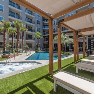 A luxurious apartment complex featuring a swimming pool, cabanas, and palm trees in a modern outdoor setting.