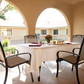 A cozy outdoor patio with a table set for a meal, surrounded by chairs under the sunlight.
