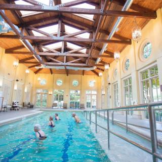 People enjoying swimming in an indoor pool with a vaulted wooden ceiling and large windows.