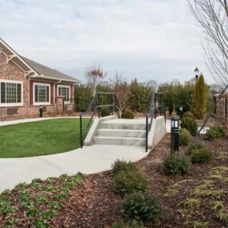A beautifully landscaped yard with a brick house, well-maintained lawn, and pathway lined with shrubs and outdoor lighting.