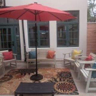 A cozy outdoor patio with colorful cushions and a red umbrella.