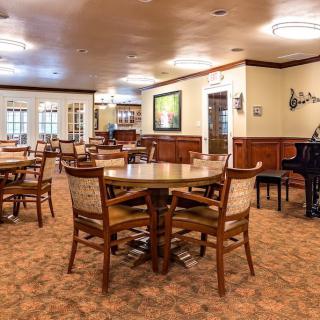 A spacious dining room with wooden tables and chairs, featuring a piano in the corner.