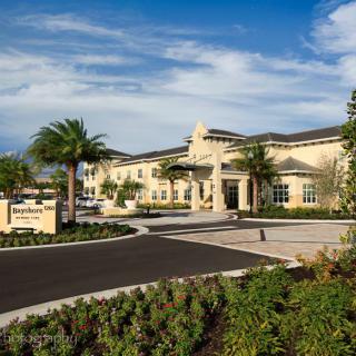 A modern residential building with palm trees and a landscaped driveway on a sunny day.