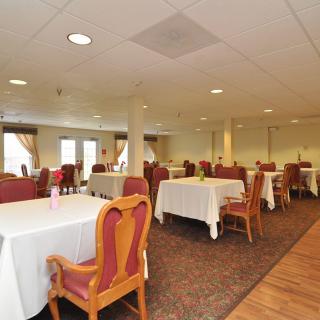A spacious dining room with tables covered in white tablecloths and surrounded by chairs.