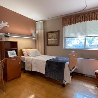 A cozy and well-lit patient room in a hospital, featuring a bed, furniture, and decorative elements.