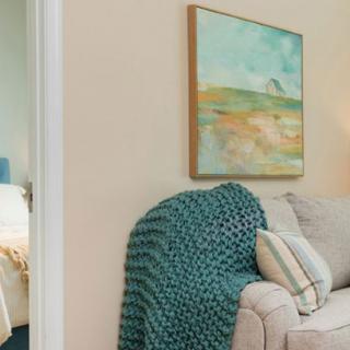 A cozy living room corner featuring a sofa with pillows and a textured blanket, complemented by a landscape painting on the wall.