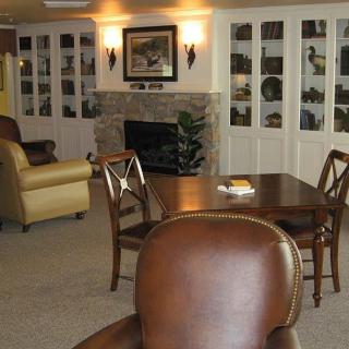 A cozy living room featuring a seating area with comfortable chairs, a wooden table, and a fireplace surrounded by bookshelves.