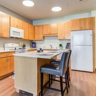 A modern kitchen featuring wooden cabinets, a central island with bar stools, and standard appliances including a microwave and refrigerator.