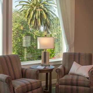 A cozy living room with two chairs and a lamp by a large window overlooking a palm tree.