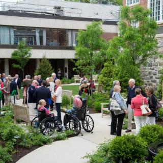 A group of people enjoying a social gathering in a garden setting, with some individuals using wheelchairs.