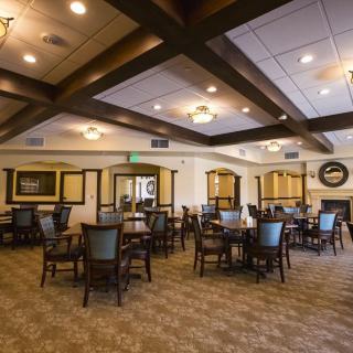 A spacious dining room with multiple tables and chairs, featuring warm lighting and a carpeted floor.