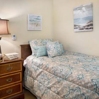 A cozy bedroom with a single bed, floral comforter, and coastal-themed wall art.