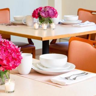 A neatly set restaurant table with bright pink flowers and elegant place settings.