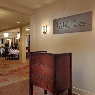 Entrance to a restaurant lobby with a wooden reception desk and visible dining area in the background.