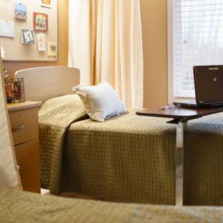 A cozy bedroom setup with a single bed and a laptop on a side table.