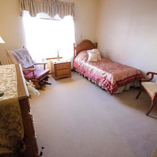 A cozy bedroom with a single bed, chair, and a window letting in natural light.