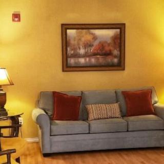 A cozy living room with a blue sofa, accented by red and striped cushions, flanked by warm lighting and decorated with a scenic painting.