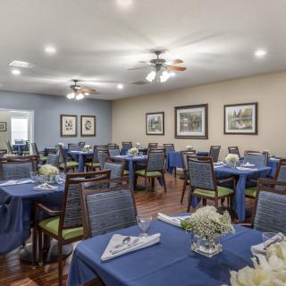 A well-arranged dining room with tables covered in blue tablecloths, surrounded by chairs and decorated with wall art.
