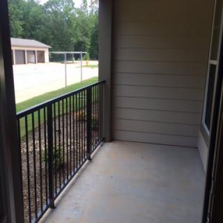A small outdoor apartment balcony with a metal railing and view of a yard.