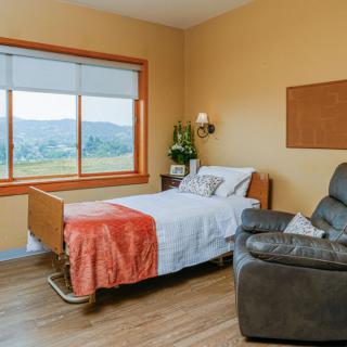 A cozy hospital room with a bed, recliner, and a large window offering a scenic landscape view.