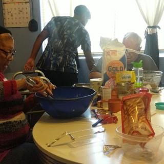 A group of people gathered around a table preparing food in a kitchen setting.