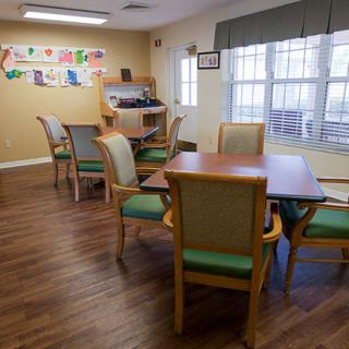 A cozy dining room featuring wooden tables and chairs, with natural light streaming through large windows.