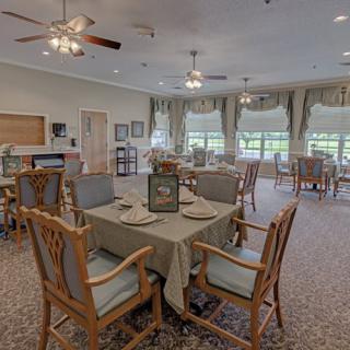 A well-decorated dining room with multiple tables and chairs, featuring large windows and ceiling fans.