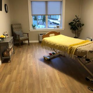 A serene healthcare room featuring a hospital bed with a yellow blanket, a comfortable chair, and natural light from the window.