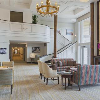 A spacious hotel lobby with a seating area, elegant chandelier, and stairway leading to an upper level.
