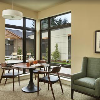 A modern dining area with large windows, a round table with chairs, and an armchair.