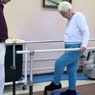 An elderly person engaging in physical therapy exercises using parallel bars for support.