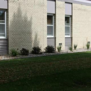 A brick building with several windows and landscaped greenery in front.