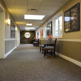 A well-lit hallway with chairs, artwork on the walls, and large windows.