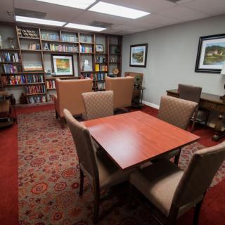 A cozy library reading room with bookshelves, a table, and chairs.